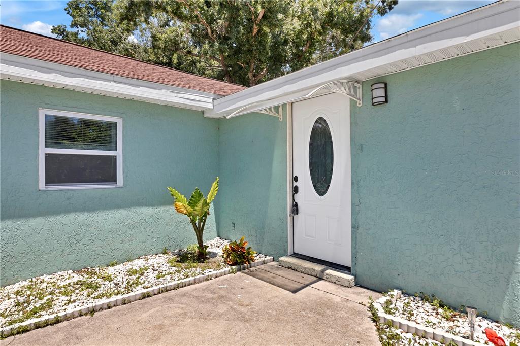 The exterior of a light green house features a white front door and a concrete patio — 2839 OLYMPIC STREET, SARASOTA, FL