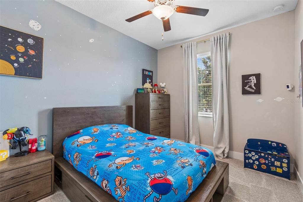 A bedroom with a bed, dresser, space-themed wall decor, and a blue toy chest — 9911 CAMPANULA COURT, LAND O LAKES, FL