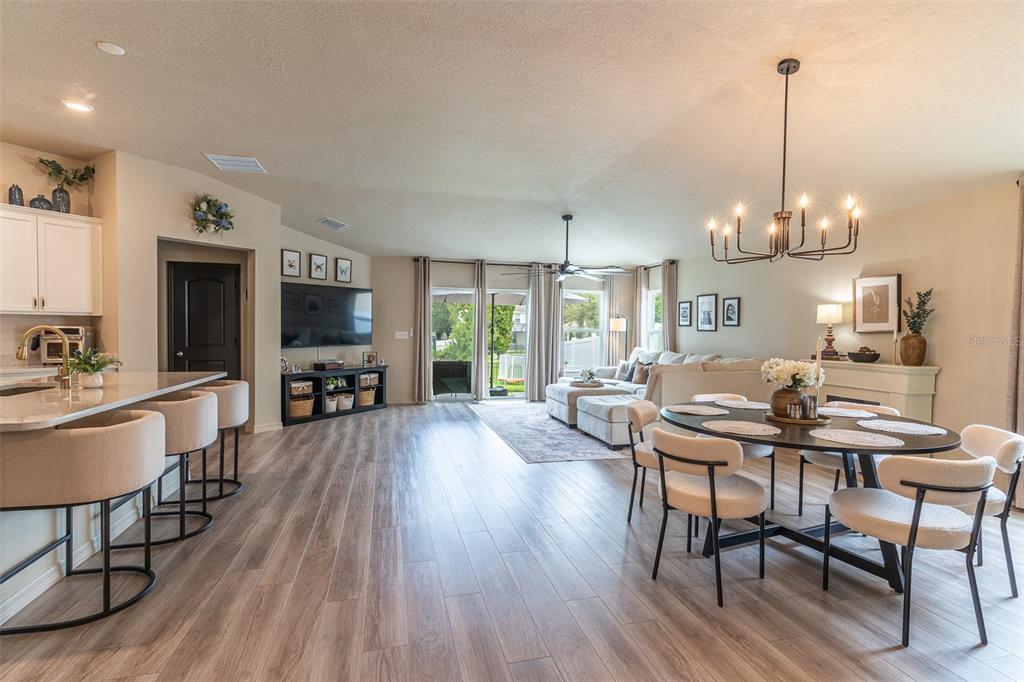An open-concept living and dining area features light wood flooring, a kitchen island, and chandelier — 615 VALRI PARK DRIVE, VALRICO, FL