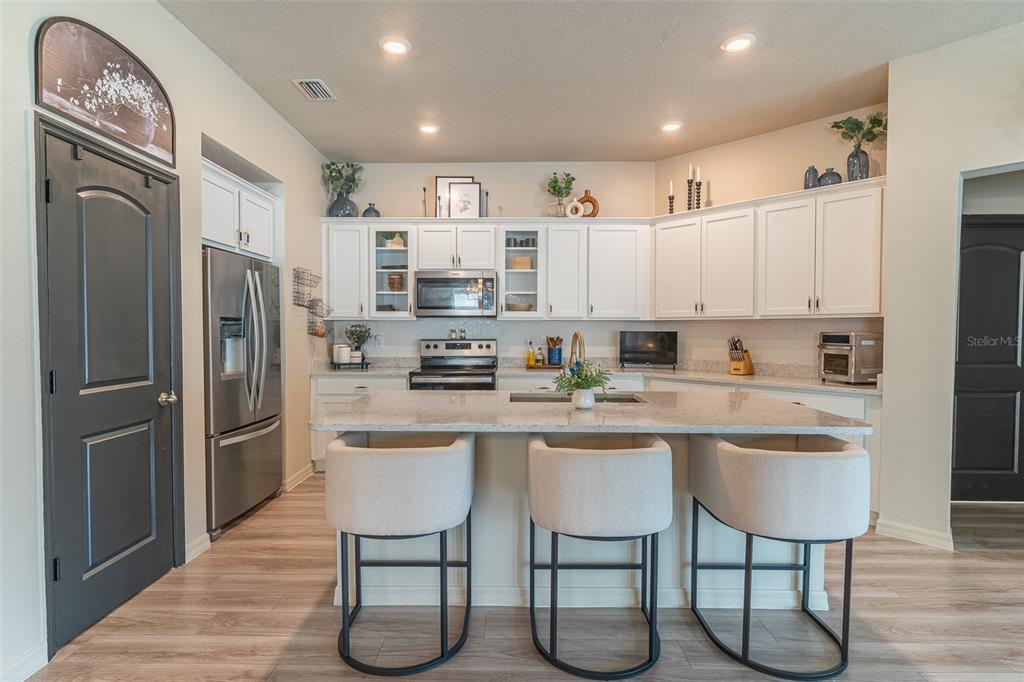 A kitchen features white cabinets, stainless steel appliances, a granite island, and three bar stools — 615 VALRI PARK DRIVE, VALRICO, FL