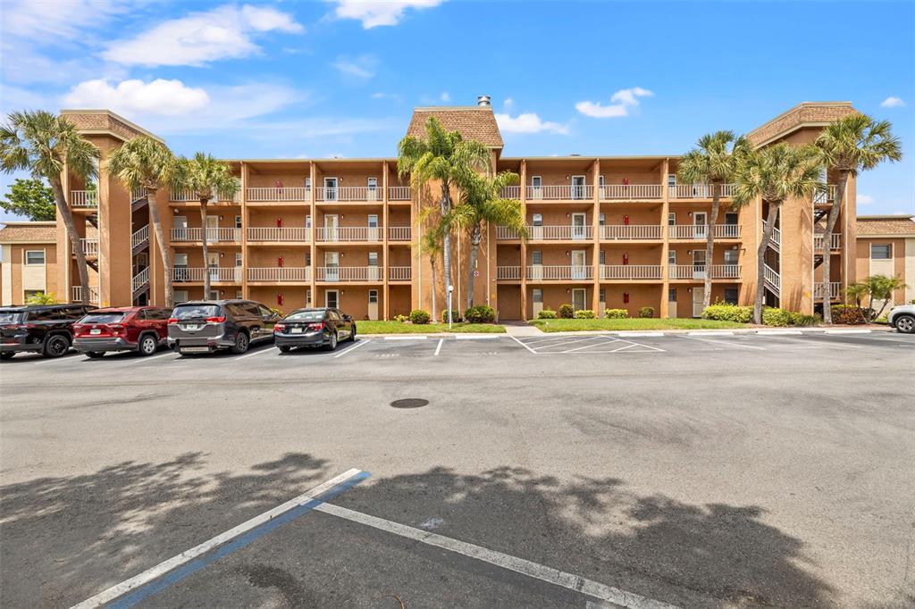 A multi-story apartment building with tan stucco walls and palm trees in the parking lot — 12760 INDIAN ROCKS ROAD UNIT 107, LARGO, FL