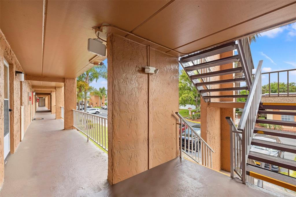 An outdoor apartment walkway features a concrete floor, stucco walls, and a metal staircase — 12760 INDIAN ROCKS ROAD UNIT 107, LARGO, FL