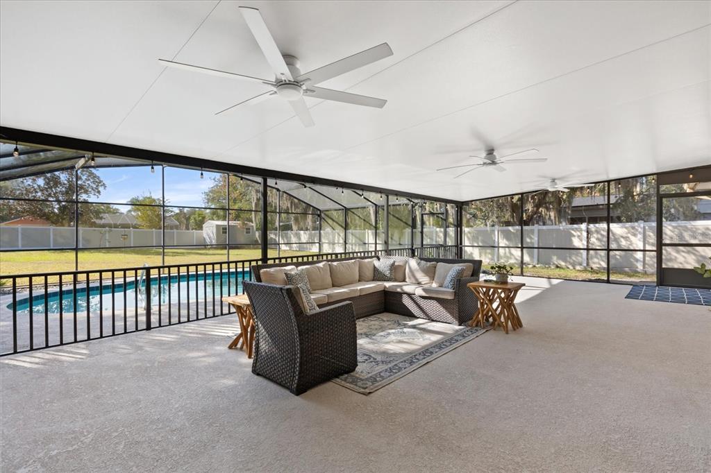 A covered patio features a pool, wicker sectional seating, and ceiling fans under a roof — 2047 ROCKY HILL DRIVE, DELTONA, FL