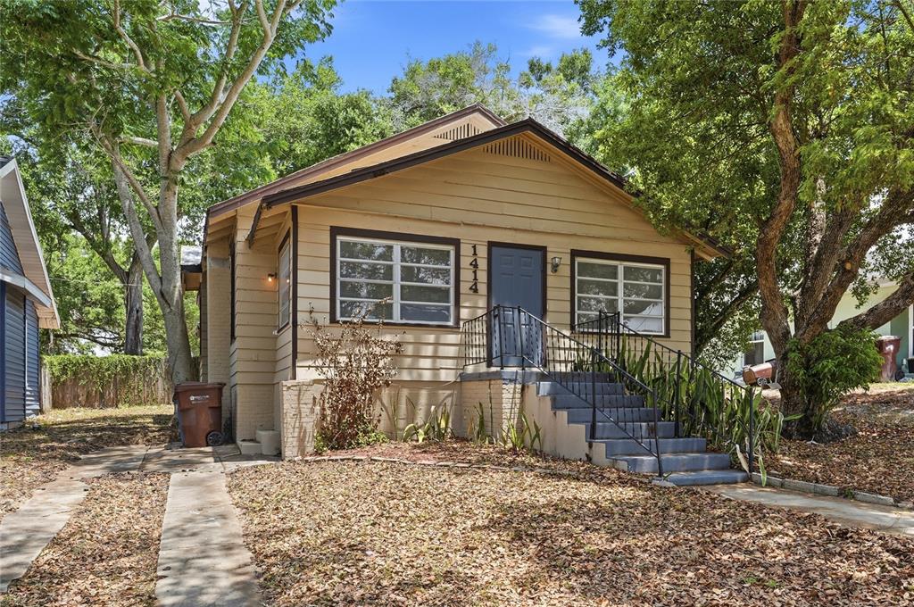 A tan, single-story house with a front porch, stairs, and a driveway sits among trees — 1414 JOHNS AVENUE, HAINES CITY, FL