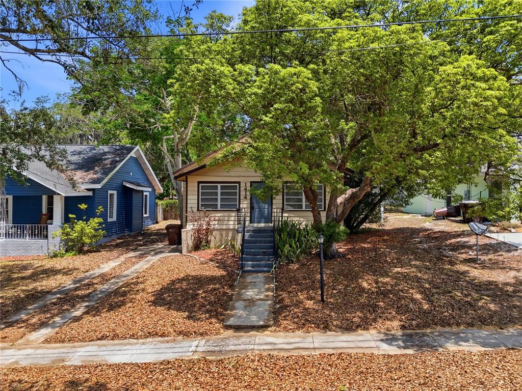 A single-story house with tan siding and a front porch sits behind a large tree — 1414 JOHNS AVENUE, HAINES CITY, FL