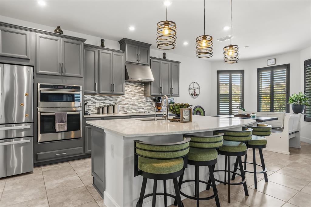 A kitchen features gray cabinets, stainless steel appliances, a quartz island, and three green stools — 3963 CARRICK BEND DRIVE, KISSIMMEE, FL