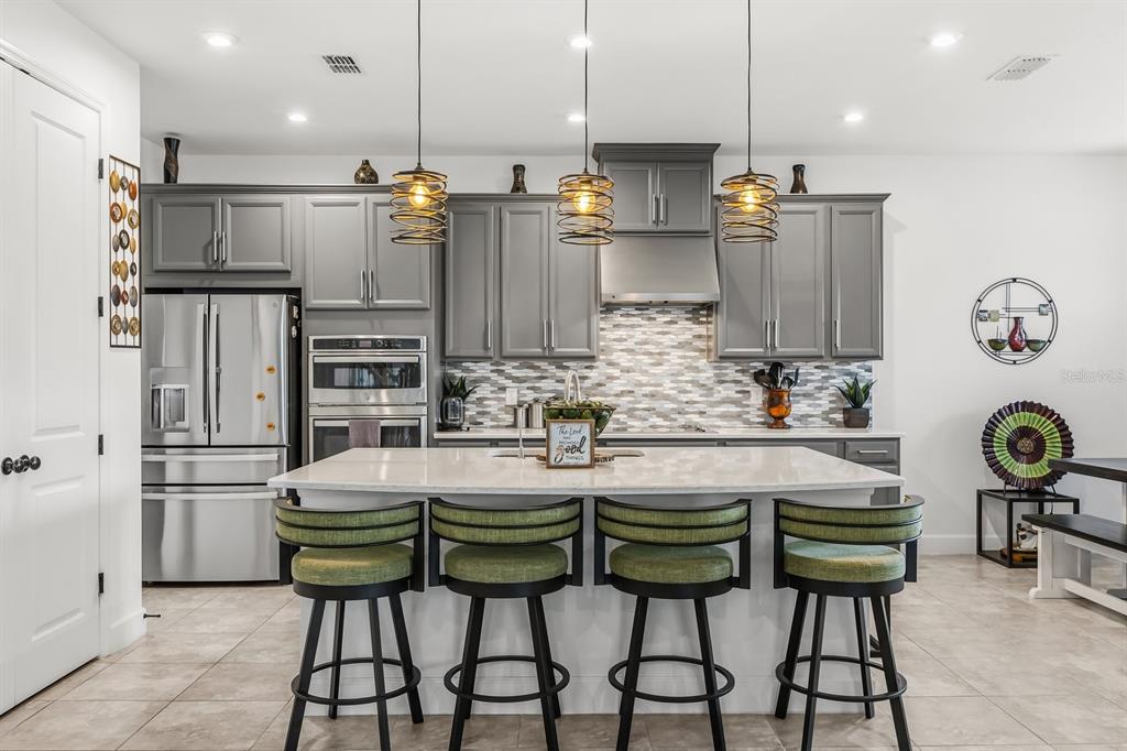A kitchen features gray cabinets, a white island with four green stools, and pendant lighting — 3963 CARRICK BEND DRIVE, KISSIMMEE, FL