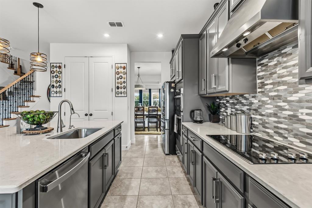 A modern kitchen features gray cabinets, a white quartz island, and a geometric tile backsplash — 3963 CARRICK BEND DRIVE, KISSIMMEE, FL