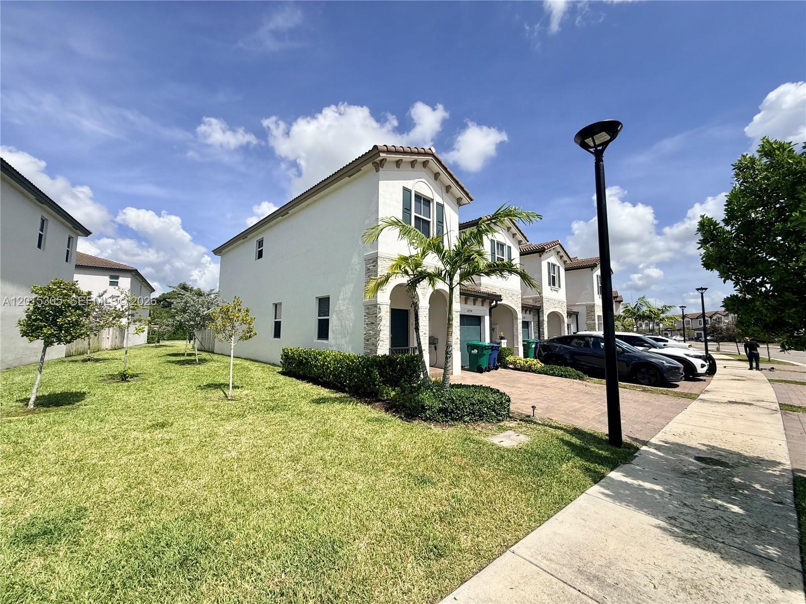 A row of two-story townhouses with white stucco exteriors, stone accents, and paved driveways — 12750 NW 23rd Pl, Miami FL 33167, MIAMI, FL