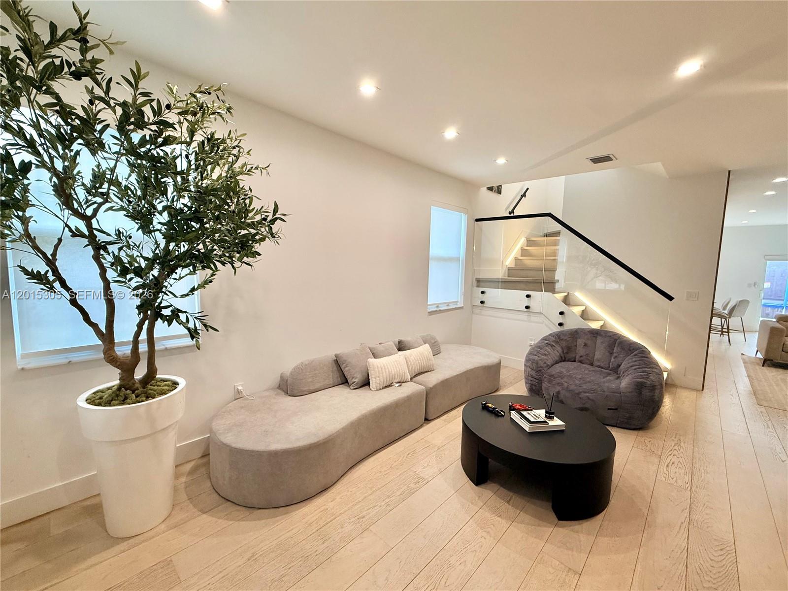 A modern living room features a grey sectional, a fuzzy chair, and a glass-railed staircase — 12750 NW 23rd Pl, Miami FL 33167, MIAMI, FL