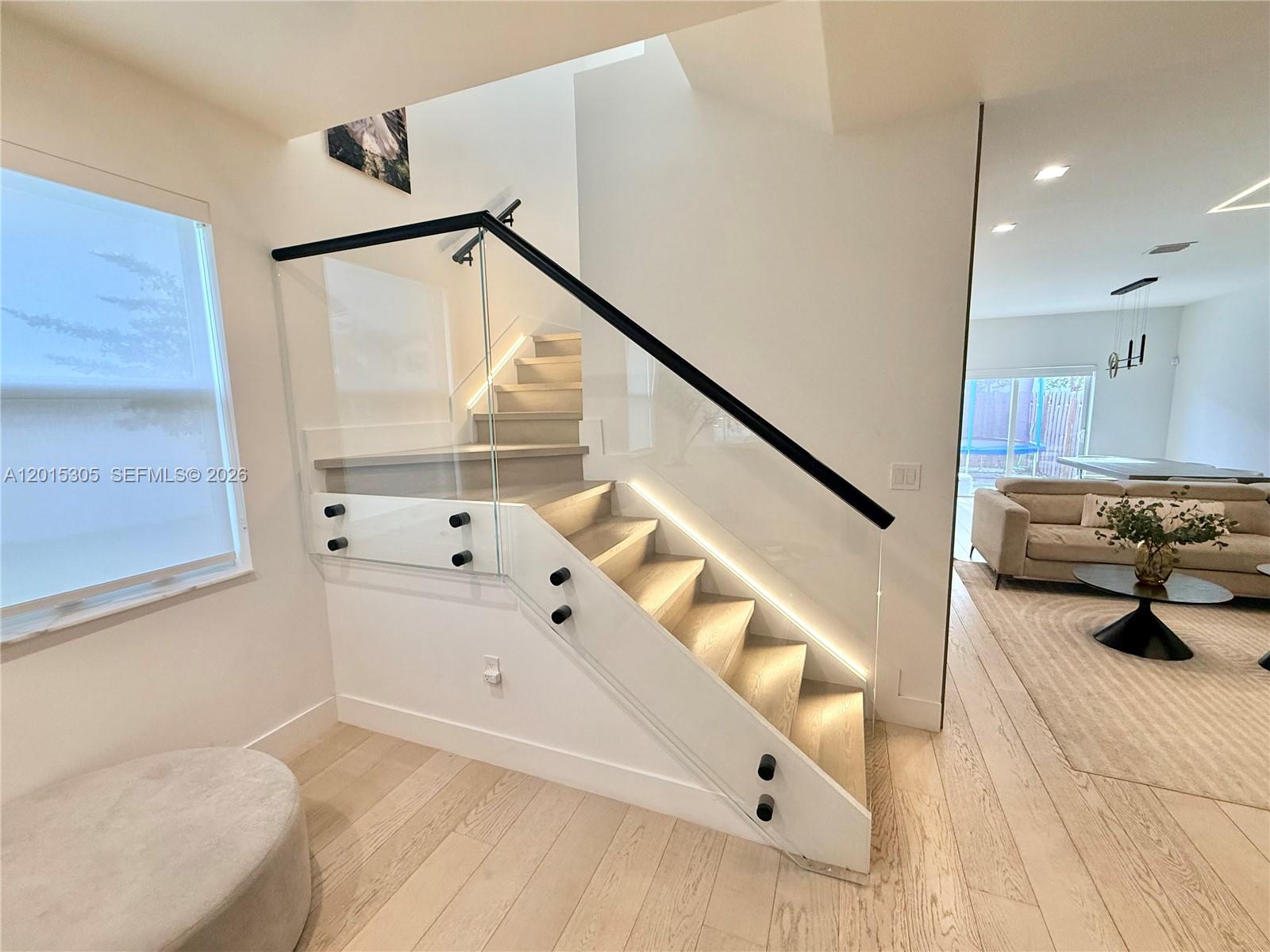 A modern staircase features glass railings, black hardware, and integrated LED lighting — 12750 NW 23rd Pl, Miami FL 33167, MIAMI, FL