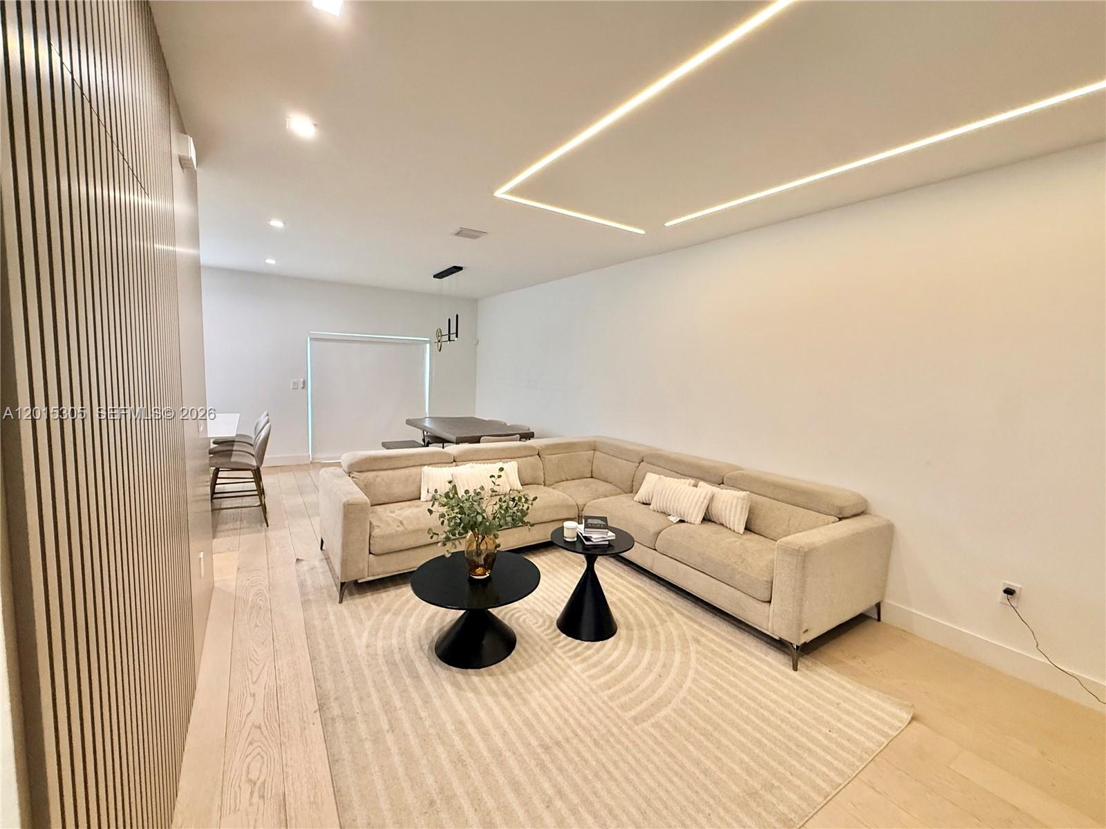 A modern living room features a beige sectional sofa, two round tables, and slatted wall paneling — 12750 NW 23rd Pl, Miami FL 33167, MIAMI, FL