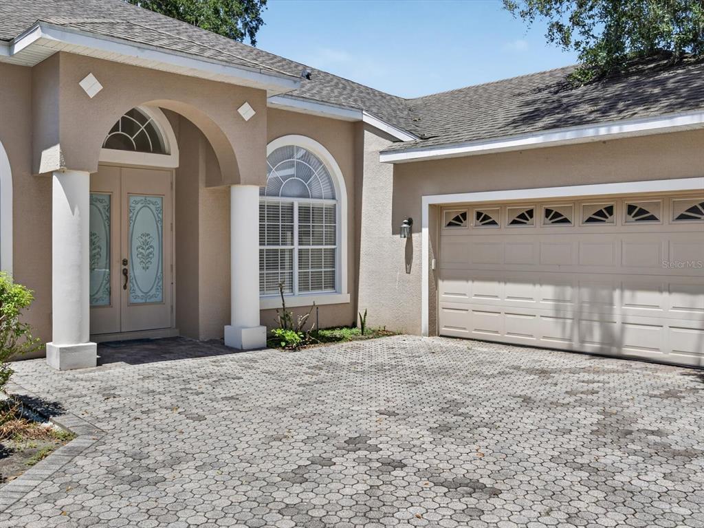 A beige house exterior features a paved driveway, a double-car garage, and an arched entryway — 2275 RAMBLING OAKS WAY, KISSIMMEE, FL
