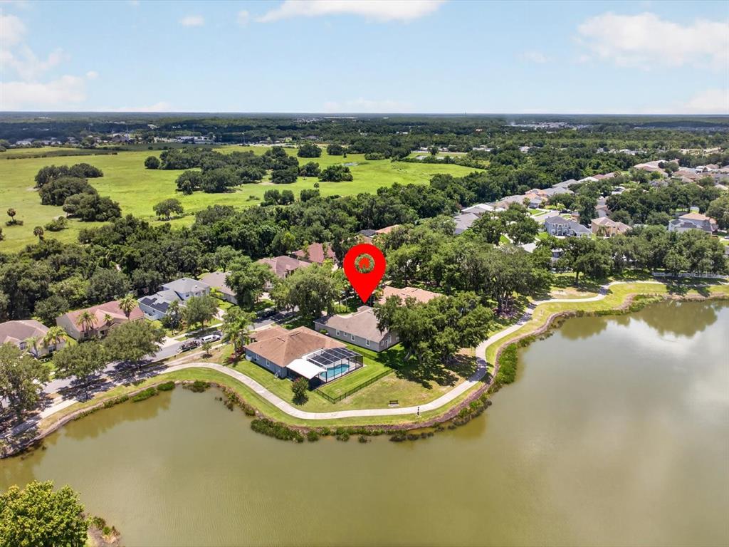 An aerial view shows a house with a pool beside a lake and walking path — 2275 RAMBLING OAKS WAY, KISSIMMEE, FL