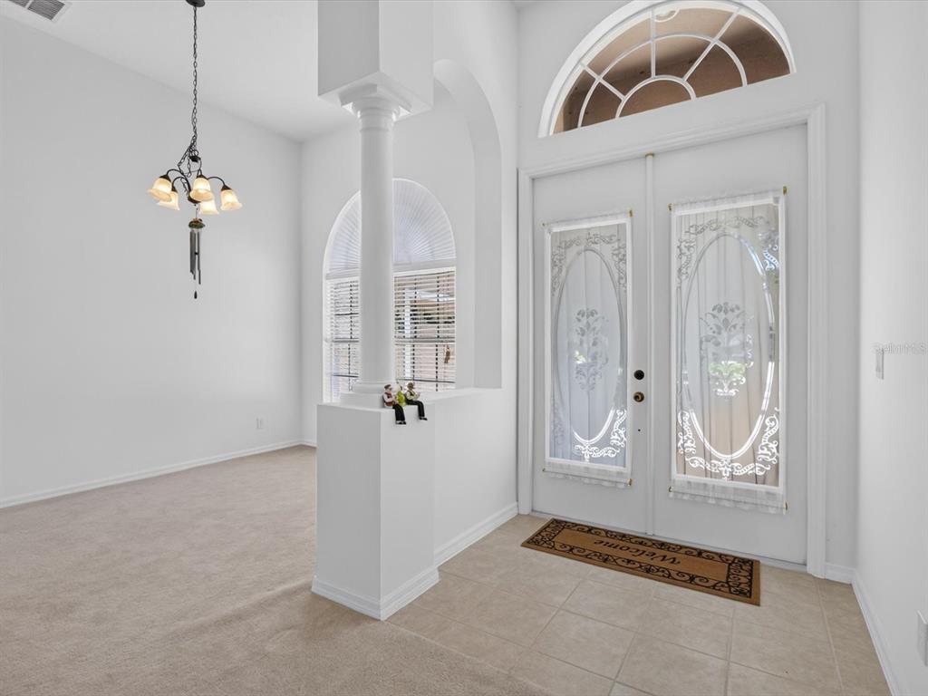 An entryway with tile flooring, a carpeted dining area, a white column, and double doors — 2275 RAMBLING OAKS WAY, KISSIMMEE, FL