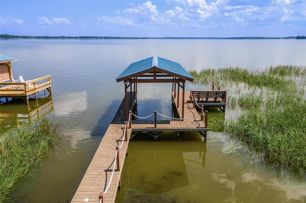 A wooden boat dock with a blue metal roof extends into a calm lake — 6274 SAILBOAT AVENUE, TAVARES, FL