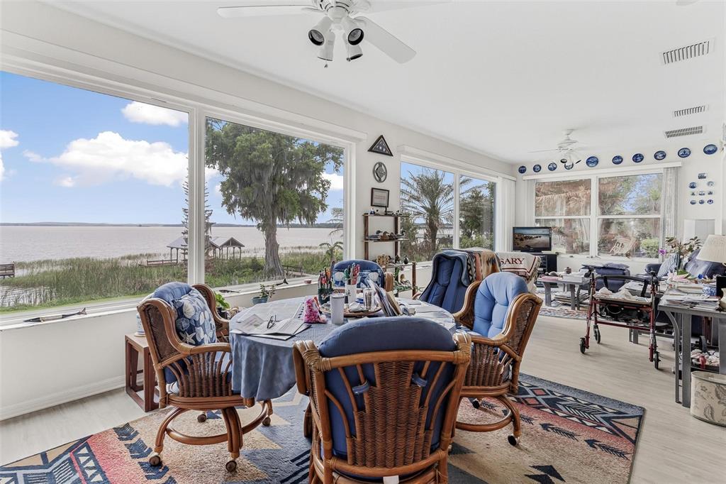 A sunroom features a dining set, a patterned area rug, and large windows overlooking a lake — 6274 SAILBOAT AVENUE, TAVARES, FL