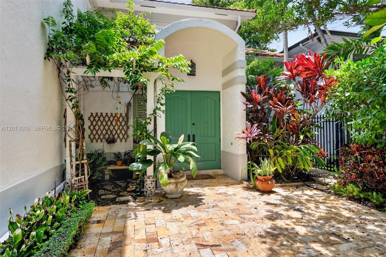A stone-paved entryway features a green double door under an arched portico with lush landscaping — 1818 Espanola Dr, Miami FL 33133, MIAMI, FL