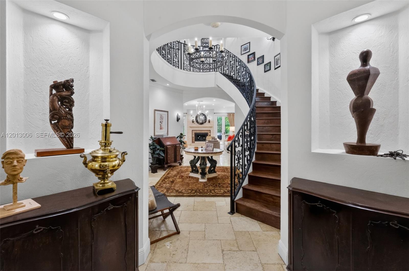 An entryway features a curved wooden staircase, stone flooring, and decorative alcoves with sculptures — 1818 Espanola Dr, Miami FL 33133, MIAMI, FL