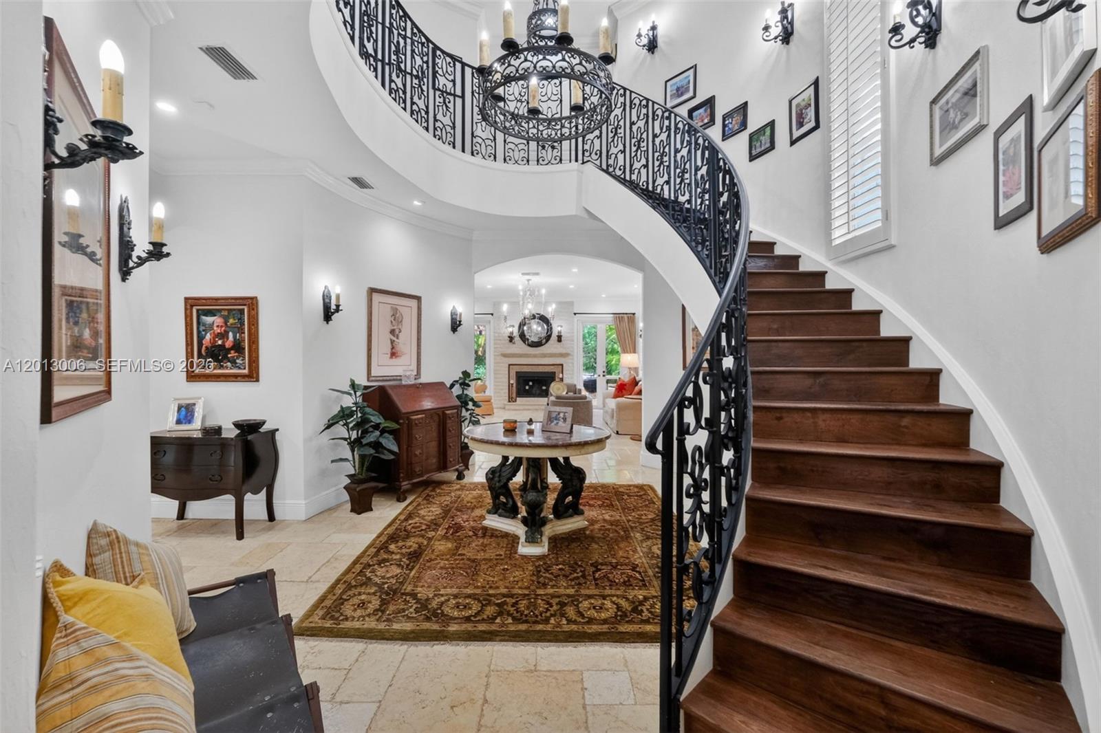 A grand foyer features a curved wooden staircase, wrought iron railing, and a central table — 1818 Espanola Dr, Miami FL 33133, MIAMI, FL