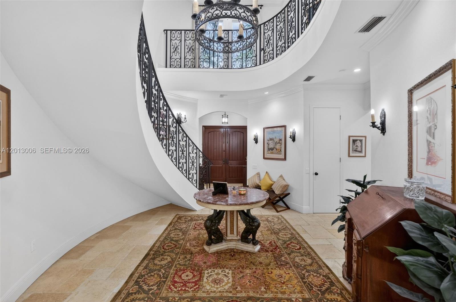 A grand foyer features a curved staircase with iron railings, stone flooring, and a chandelier — 1818 Espanola Dr, Miami FL 33133, MIAMI, FL
