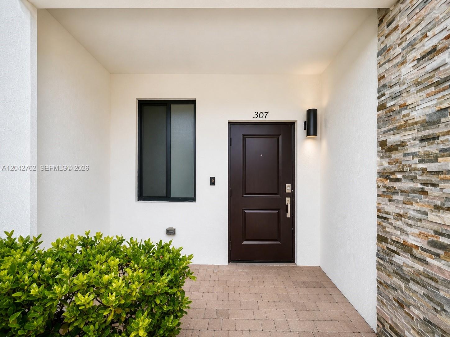 The exterior entryway features a dark brown door, a window, and a stone accent wall — 307 NE 208th Ter, Miami FL 33179, MIAMI, FL