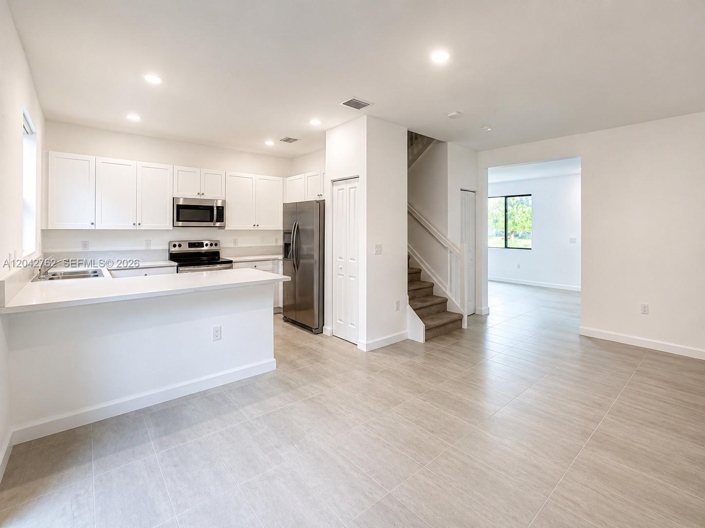 A modern kitchen with white cabinets and stainless steel appliances opens to a living area — 307 NE 208th Ter, Miami FL 33179, MIAMI, FL