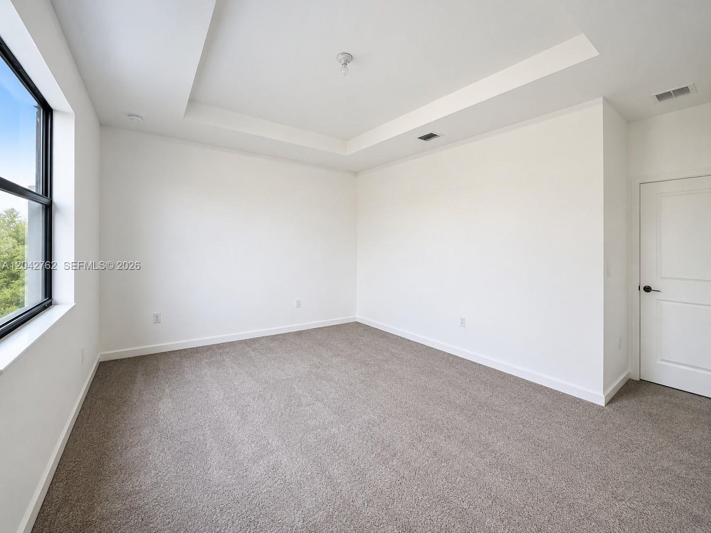 An empty bedroom features white walls, gray carpeting, a tray ceiling, and a window — 307 NE 208th Ter, Miami FL 33179, MIAMI, FL