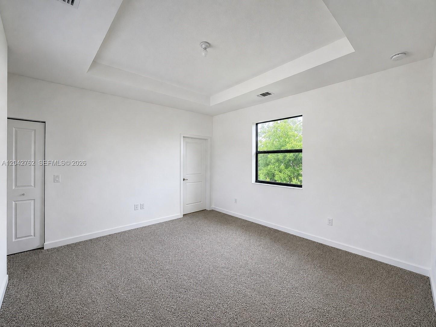 An empty bedroom features white walls, a tray ceiling, carpeted flooring, and a single window — 307 NE 208th Ter, Miami FL 33179, MIAMI, FL