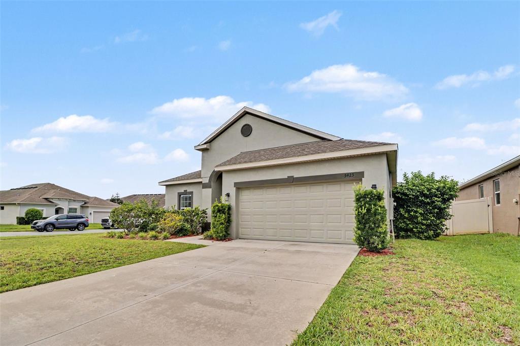 A tan single-story house with a two-car garage and a concrete driveway — 5423 DOVE COTTAGE LN, ST CLOUD, FL