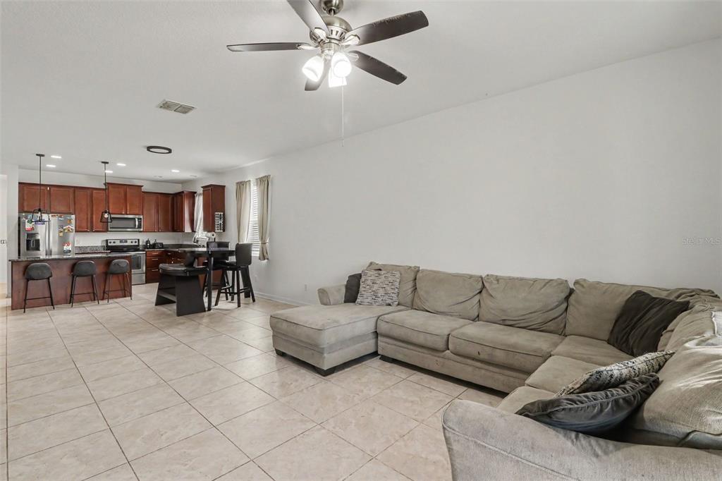 An open-concept living room with tile floors and a sectional sofa faces a kitchen area — 5423 DOVE COTTAGE LN, ST CLOUD, FL