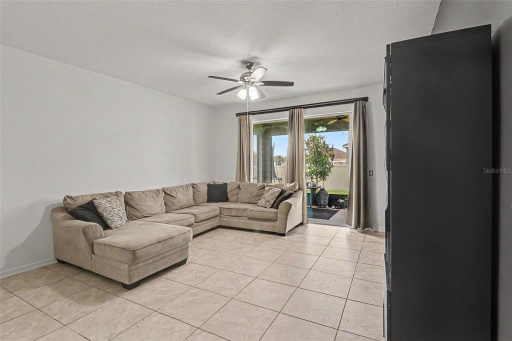 A living room features a large sectional sofa, tile flooring, and sliding glass patio doors — 5423 DOVE COTTAGE LN, ST CLOUD, FL