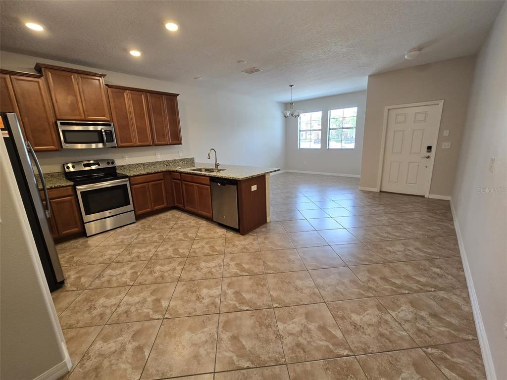 A kitchen with wood cabinets, stainless steel appliances, and tile flooring opens to a living area — 4252 FENNWOOD COURT, WESLEY CHAPEL, FL