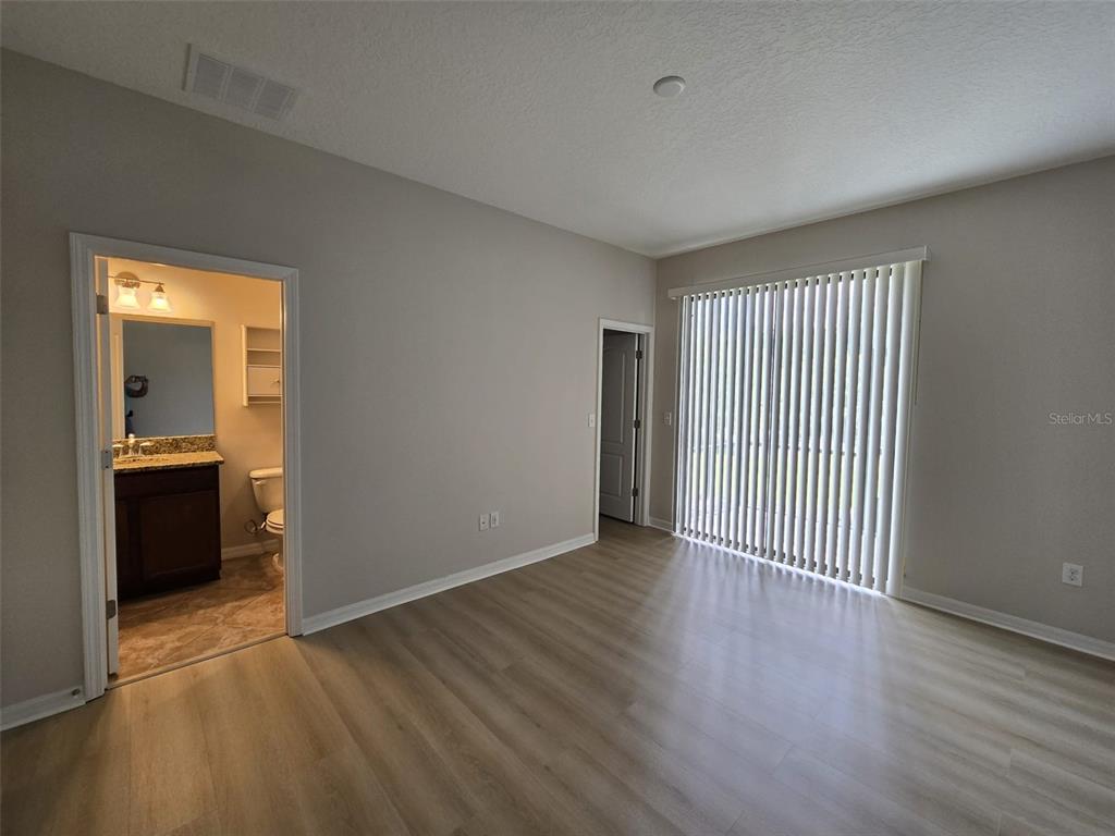 An empty bedroom features light wood-look flooring, a sliding glass door, and an attached bathroom — 4252 FENNWOOD COURT, WESLEY CHAPEL, FL