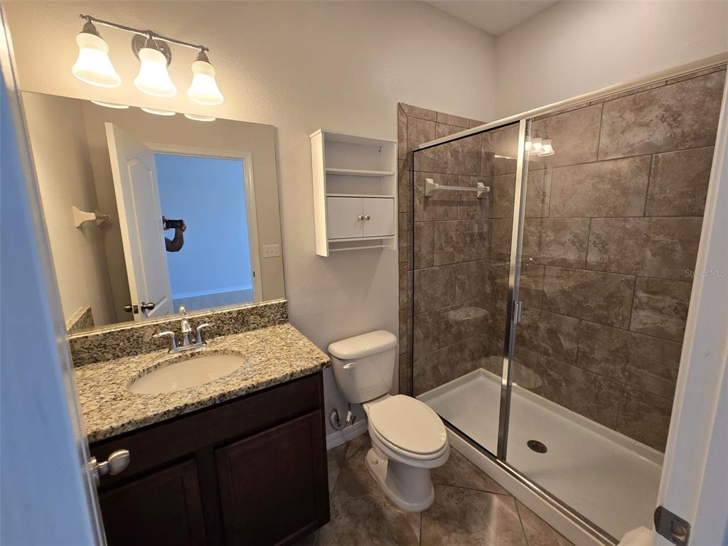 A bathroom features a granite vanity, a walk-in shower with tiled walls, and a toilet — 4252 FENNWOOD COURT, WESLEY CHAPEL, FL
