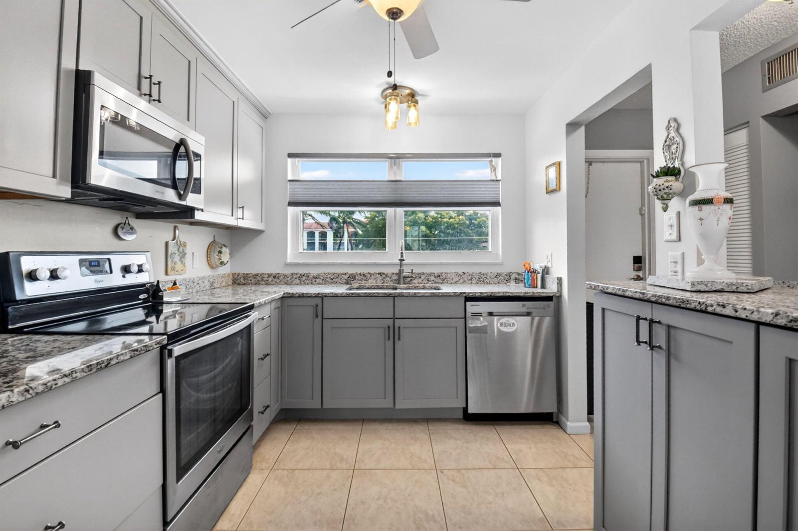 A kitchen features gray cabinets, stainless steel appliances, granite countertops, and light-colored tile flooring — 2016 S Federal Highway # E309, Boynton Beach FL 33435, BOYNTON BEACH, FL