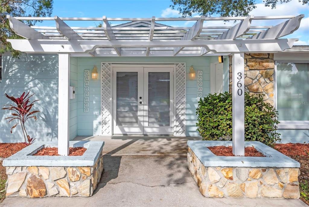 A light blue house exterior features a white pergola over a double-door entrance with planters — 360 57TH STREET N, ST PETERSBURG, FL