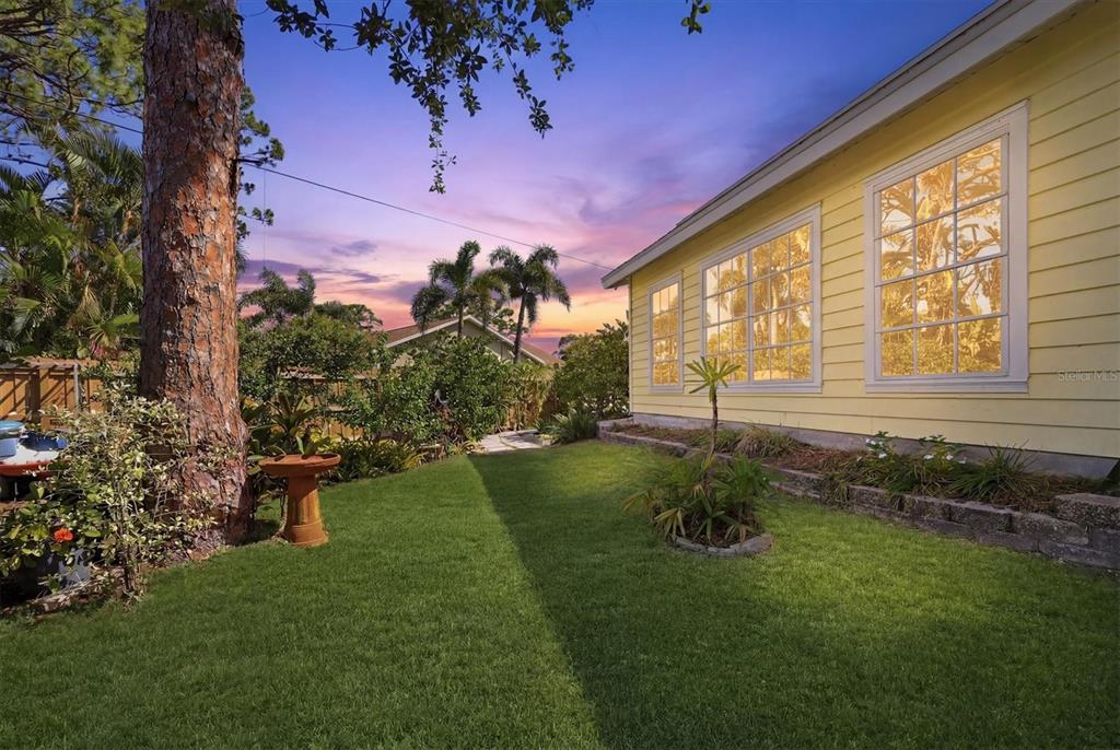 A yellow house exterior with large windows overlooks a grassy lawn at sunset — 4821 EGRET ROAD, VENICE, FL