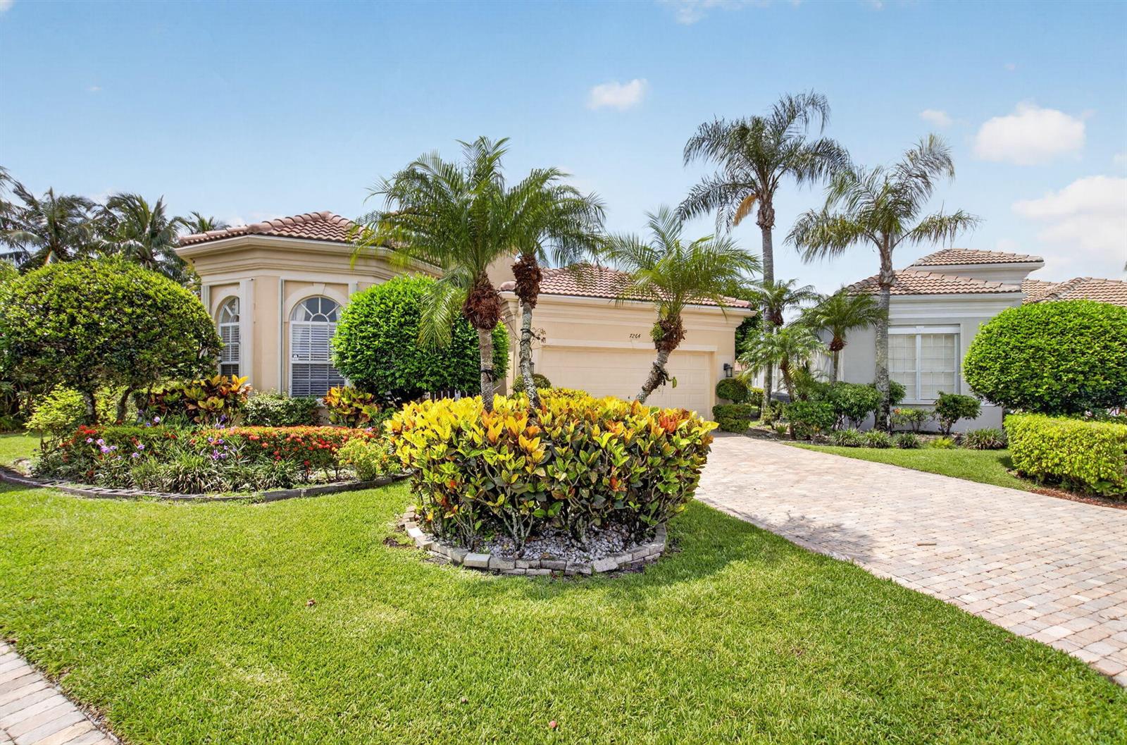 A single-story house with a paved driveway, palm trees, and manicured landscaping under a blue sky — 7264 Cataluna Circle, Delray Beach FL 33446, DELRAY BEACH, FL