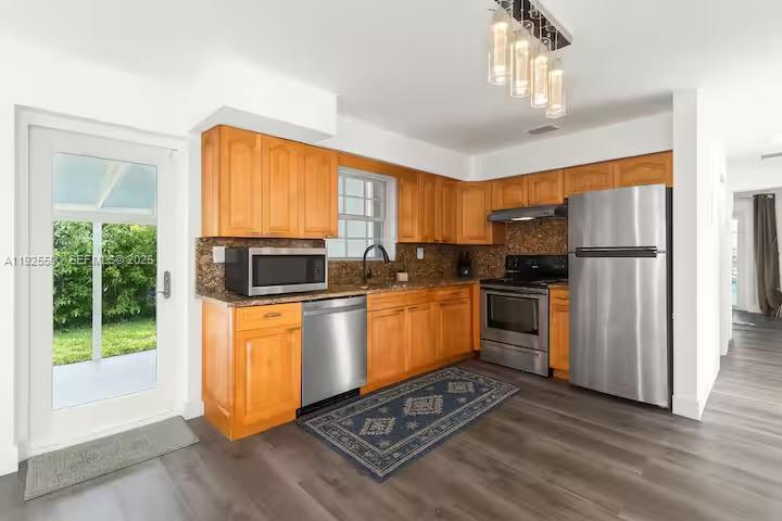 A kitchen features wooden cabinets, stainless steel appliances, and a patterned rug on gray flooring — 909 NE 7th St, Pompano Beach FL 33060, POMPANO BEACH, FL