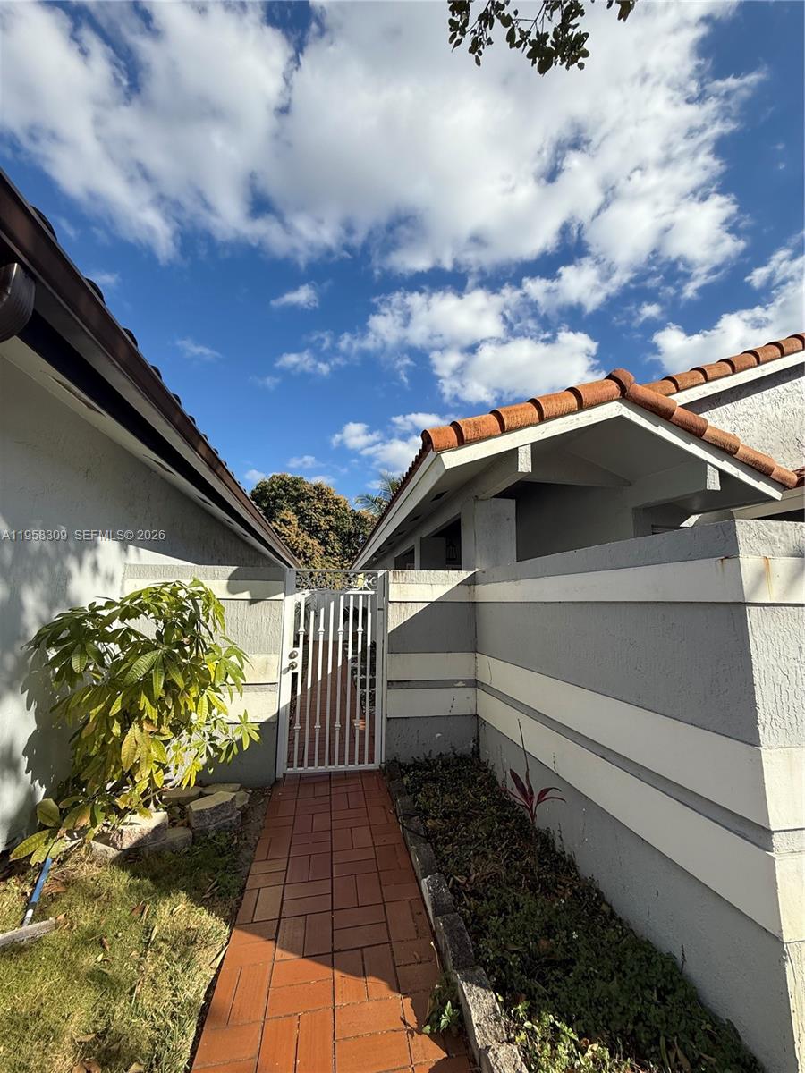 A brick walkway leads to a white metal gate between two stucco exterior walls — 18237 NW 61st Pl, Hialeah FL 33015, HIALEAH, FL