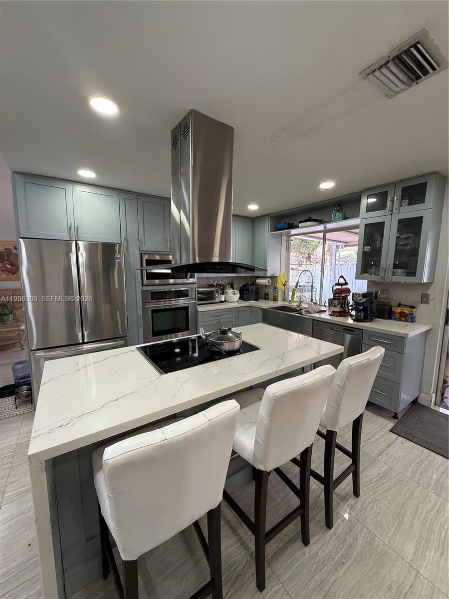 A kitchen features light blue cabinets, a central island with a cooktop, and stainless appliances — 18237 NW 61st Pl, Hialeah FL 33015, HIALEAH, FL