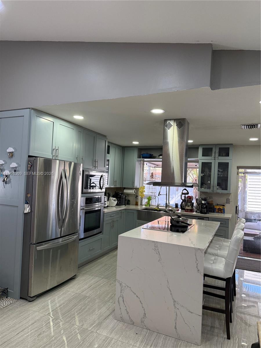 A kitchen features sage green cabinets, a marble-topped island, and stainless steel appliances — 18237 NW 61st Pl, Hialeah FL 33015, HIALEAH, FL