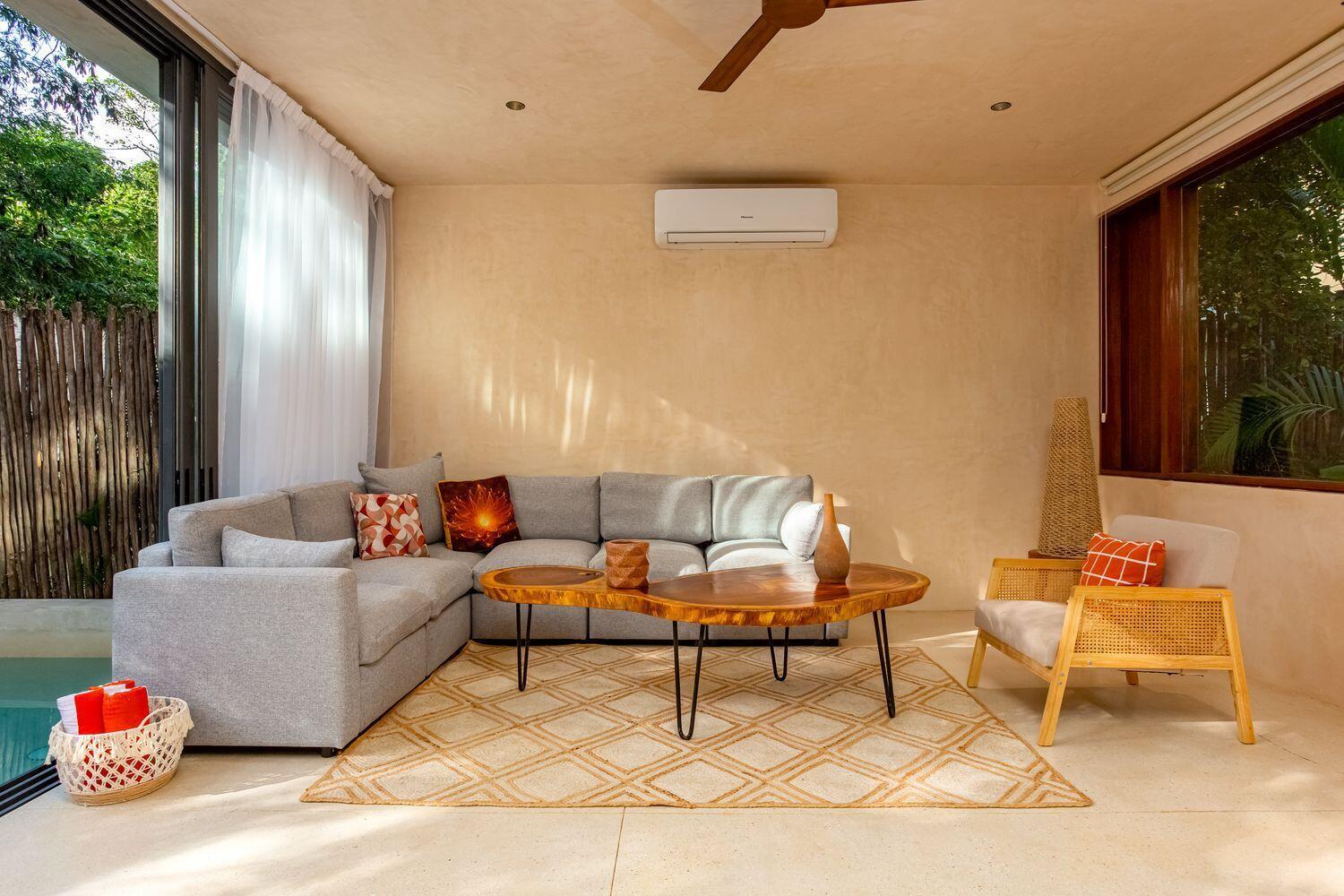 A living room features a grey sectional sofa, a wood coffee table, and a cane chair — Amari Tulum 10 Avenida Norte & Calle Palma, FL