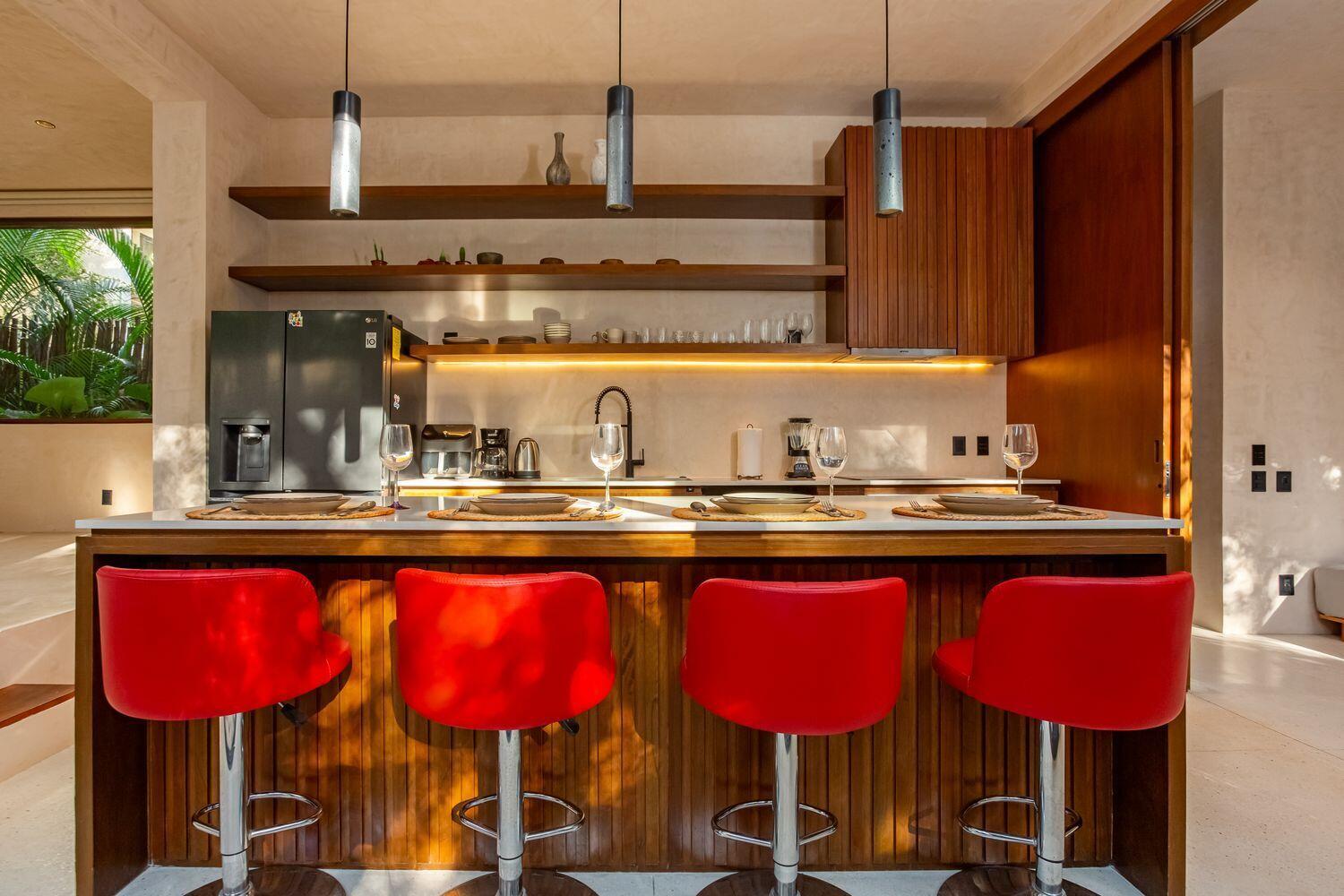 A kitchen island with four red bar stools sits before open shelving and wooden cabinetry — Amari Tulum 10 Avenida Norte & Calle Palma, FL