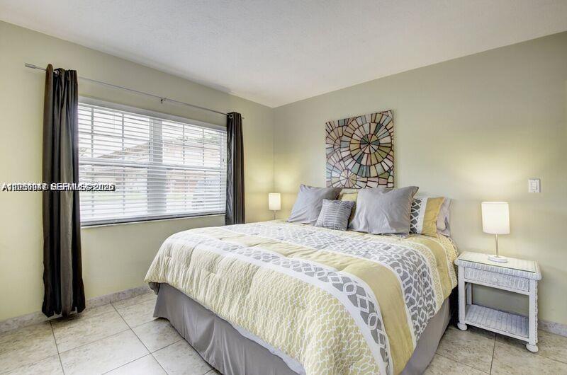 A bedroom features a bed with a patterned comforter, two nightstands, and a large window — 221 SE 9th Ave # 112, Pompano Beach FL 33060, POMPANO BEACH, FL