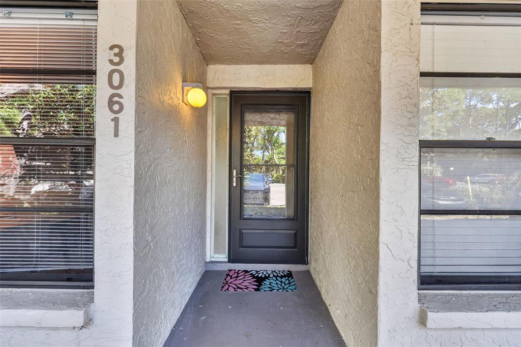 A front entryway features a dark storm door, a wall-mounted light, and house numbers — 3061 QUAIL HOLLOW UNIT # 35, SARASOTA, FL