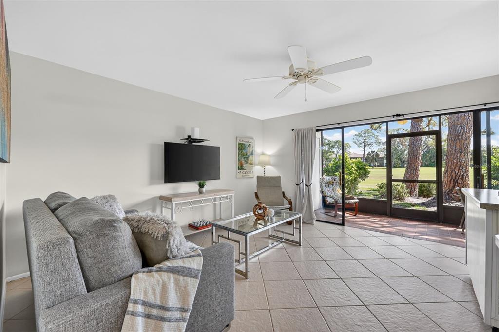A living room features a gray sofa, glass coffee table, wall-mounted television, and sliding glass doors — 3061 QUAIL HOLLOW UNIT # 35, SARASOTA, FL