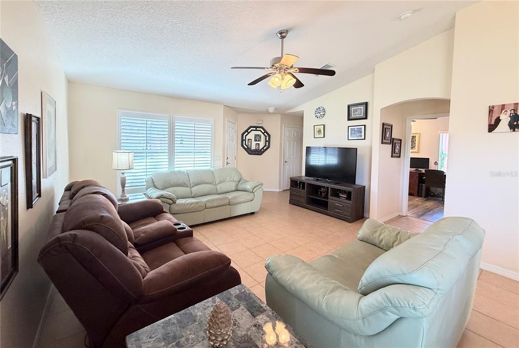 A living room features tile flooring, a ceiling fan, and three sofas arranged around a television — 537 GRAND CANAL DRIVE, POINCIANA, FL