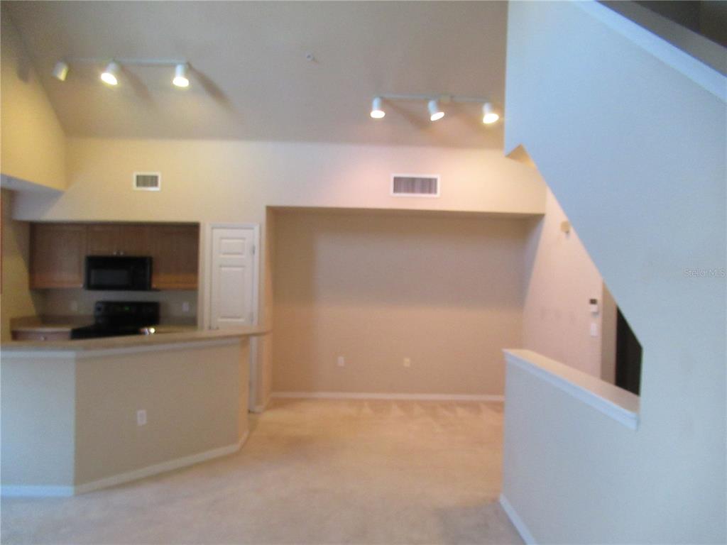 A carpeted living area features a kitchen counter, track lighting, and a staircase — 5601 ROSEHILL ROAD UNIT 203, SARASOTA, FL